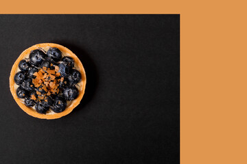 A flat lay of blueberry tartlet on a black orange background. Copy space.
