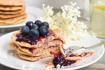 Stack of healthy oat pancakes served with elder flower, blueberry jam and fresh berries.