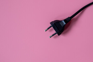 Black electrical plug and electrical cord pink background.