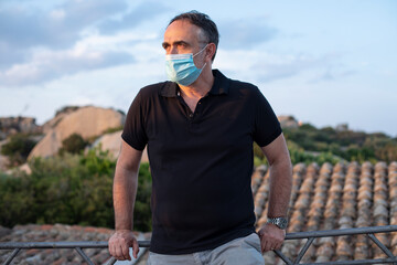Uomo moro in vacanza con la mascherina chirurgica vestito casual con un maglietta nera si rilassa in un villaggio immerso nella natura 