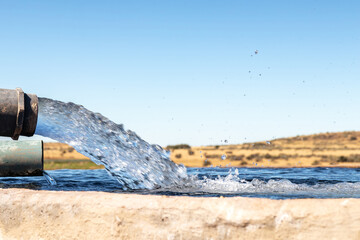 A Large stream of water gushing out of a pipe and filling a cement farm dam closeup