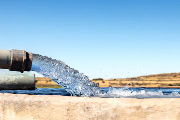 A Large stream of water gushing out of a pipe and filling a cement farm dam closeup