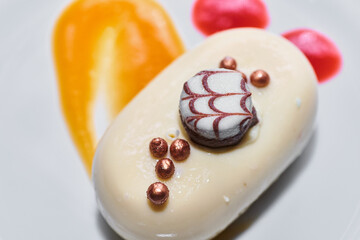Closeup shot of romantic luxurious pastry dessert. Small individual portion of trendy mousse filled mini no bake cake coated with smooth white chocolate. Nicely decorated with sweet details and sauce