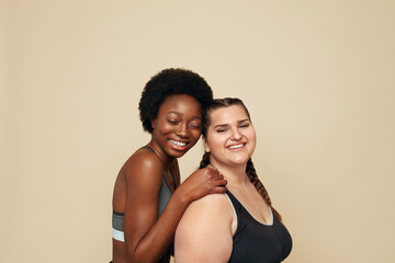 Diversity. Fitness Girls Of Different Ethnicity Portrait. Caucasian And African Models In Fitness Clothes Posing Against Beige Background. Body Positive As Lifestyle.