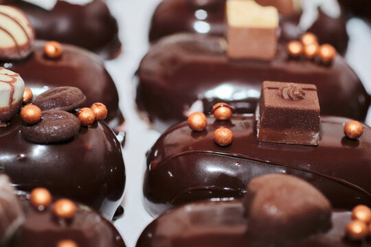 Closeup shot of mini mirror dark chocolate glazed mousse gourmet dessert. Luxurious pastry. Decorated with chocolate details. Sweet appetizer in individual small portions.