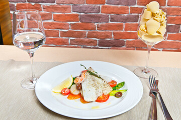Warm salad with asparagus, prawns and codfish fillet. on a white plate. with a glass of water