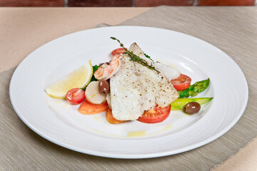 Warm salad with asparagus, prawns and codfish fillet. on a white plate. close-up view