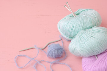 Skeins of blue lilac and turquoise yarn with knitting needles lie on the surface of the pink color