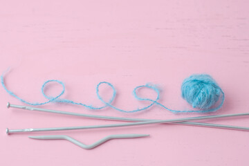 A small blue skein of mohair wool lies on the pink surface next to the knitting needles the thread is looped