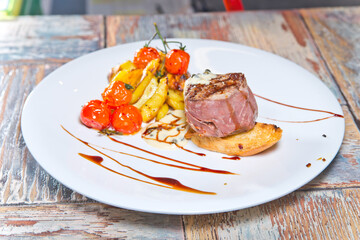 Beef medallion with fried potatoes and sun-dried tomatoes. on a white plate. on a wooden background