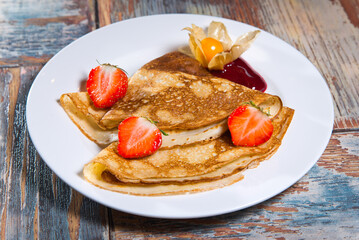 pancakes with strawberry jam and fresh strawberries. on a white plate. on a wooden background