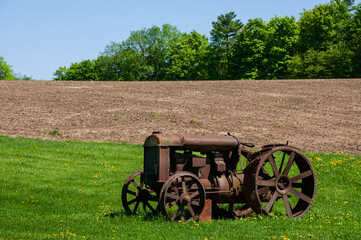 Old rusty abandoned antique farm tractor beside a plowed field