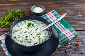 Cold soup with fresh cucumbers, radishes with yogurt in a bowl on wooden background. Traditional Russian food - okroshka. Vegetarian food. Healthy eating concept.