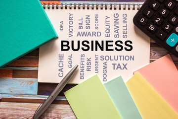 Business words on a white sheet and wooden table with a calculator, stickers and notepad