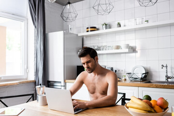 handsome shirtless freelancer working on laptop on kitchen with fruits and coffee