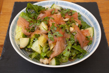 A salad with smoked salmon and mixed greens with a salad dressing and mixed herbs