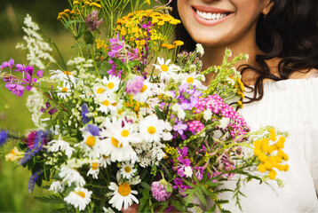 Summer lifestyle portrait of beautiful brunette woman smiling and holding bouquet of wild flowers. Enjoying sun. Happiness and love concept. Beautiful flowers. Romantic mood. Beautiful smile