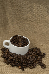 Freshly made coffee in a white cup surrounded by coffee beans on a wooden table. Fresh coffee.