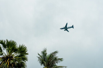 Fototapeta na wymiar Plane flying in a cloudy sky and preparing to land on a tropical island.