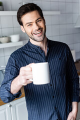 cheerful handsome man holding cup of coffee at home on quarantine