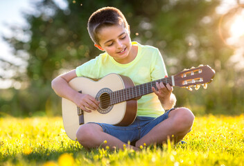 Boy playing acoustic guitar in a field at sunset