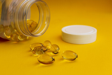 Open bottle with omega 3 pills next to it, yellow background, selective focus, free copy space