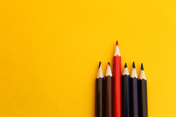 "Stand out" concept: Red pencil between the dark ones, yellow background, selective focus, free copy space