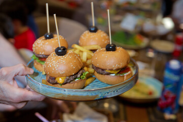 Waiter carrying a tray of appetizers. Outdoor party with finger food, burgers, sliders. man hold tray with burger at restaurant. Men's hands hold a tray with a cheeseburger. Catering service.