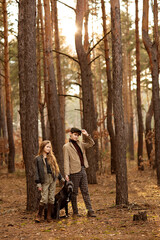Fototapeta premium Girl and boy walk with a dog Cane corso in the forest and have a fun. Children stand near a tree and hold a dog on a leash.