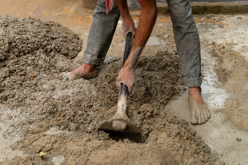 Indian labour mixing cement and water manually on floor using a shovel. Stock image.