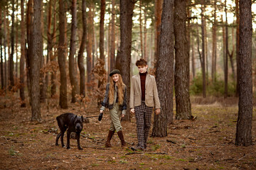 Fototapeta premium Girl and boy walk with a dog Cane corso in the forest and have a fun. Children stand near a tree and hold a dog on a leash.