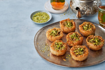 Middle eastern arab sweet pastry baklava with honey, pistachios, mint tea on a light background, selective focus. Ramadan, Eid concept.