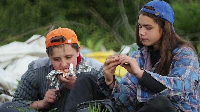 Homeless children eat food in a landfill. Two teenage bum eating a sandwich found in the trash.