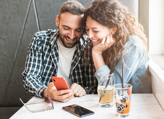 Engaged couple enjoying time together using smartphone - Friends are having fun in a bar with mobile phone.