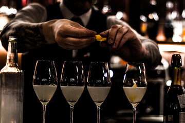 multiple champagne glasses with cocktails inside and bartender adding an orange zest 