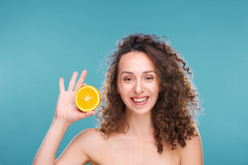 Happy young woman with dark long curly hair holding half of fresh juicy orange