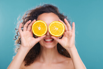 Young happy beautiful woman holding two halves of juicy orange by her eyes