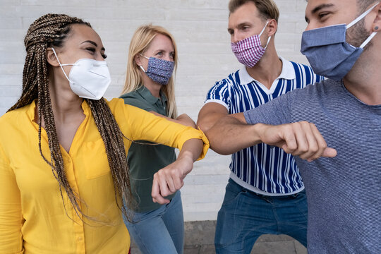 Group of young friends haveing fun and wearing protective face masks - Friends say hello with their elbows and laughing - Health care and follow measures