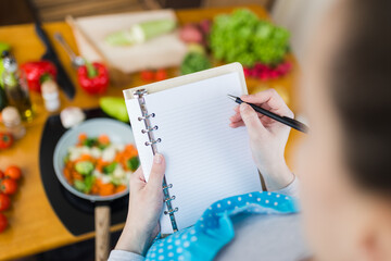 Close up of young housewife taking notes in notebook. Vegetarian food preparation concept.