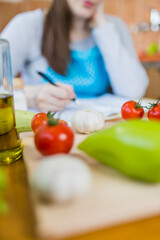 Housewife sitting at kitchen table and reading or taking notes of healthy cooking recipe.