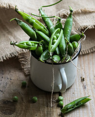 green pea pods in a mug on a wooden table