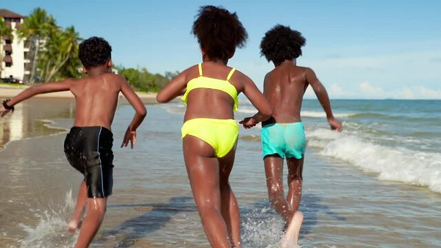 African American children race on the beach in the summer.
