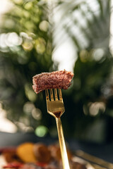 Slices of beef steak on gold fork blure background