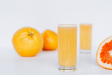 Glass with grapefruit juice and whole and sliced grapefruit on the background