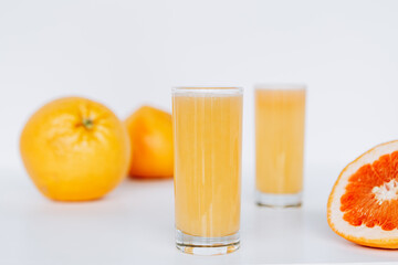 Glass with grapefruit juice and whole and sliced grapefruit on the background
