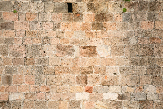Limestone wall texture. Wall of an old building with a small window and a little overgrown with grass. Abstract background.