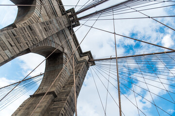 Iconico puente de Brooklyn en Nueva York, Usa. Arquitectura a gran escala de piedra con bandera ddel pais sobre cielo parcialmente nubado azul. 