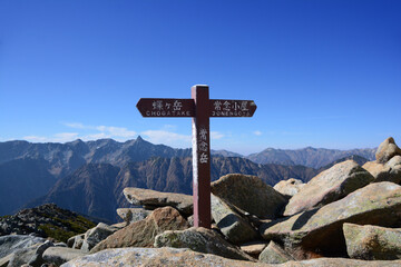 常念岳山頂の道標と槍ヶ岳（やりがたけ 3190m）。北アルプス、常念岳（じょうねんだけ 2857m）の頂上の道しるべと、遠くには、左から穂高連峰、大キレット、槍ヶ岳、東鎌尾根、三俣蓮華岳、鷲羽岳、水晶岳、と続く山並み。Mt.Yaarigatake. from the moutaintop of Mt.Jounendake. in the nothernalps.