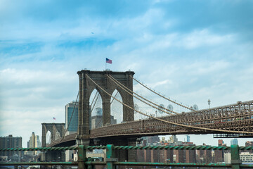 Fototapeta na wymiar Iconico puente de Brooklyn en Nueva York, Usa. Arquitectura a gran escala de piedra con bandera ddel pais sobre cielo parcialmente nubado azul. 