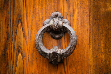Antique round metal handle on a wooden front door. Beautiful brown color elegant entrance handle on the door. Vintage metal object isolated on wooden background. Close up shot. Front view.